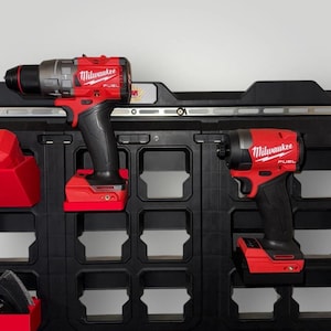 May include: Two red and black Milwaukee FUEL power tools, a drill and an impact driver, are mounted on a black storage system. The tools are cordless and feature the Milwaukee logo. The background is a neutral gray.