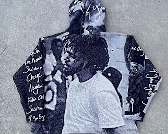 May include: A black and white woven hoodie featuring a large portrait of a person with curly hair on the front. The sleeves and hood display handwritten-style text including phrases like Ville Mentality, Change, Neighbors, and 4 Your Eyez Only.