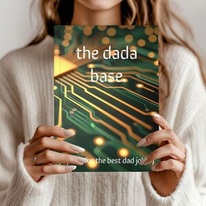 May include: A notebook with the text "the dada base" in white, set against a green and gold circuit board design. The bottom of the notebook reads "For the best dad jokes".
