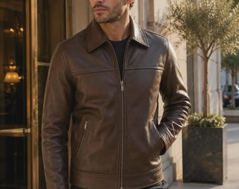 Puede incluir: Una chaqueta de cuero marrón oscuro con cuello clásico, cremallera frontal completa y dos bolsillos laterales con cierre de cremallera. La chaqueta tiene un acabado liso, mangas largas con puños y un detalle de costura horizontal en el pecho.
