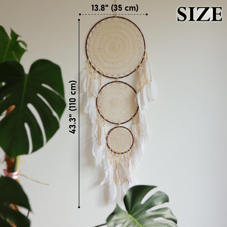 May include: A cream-colored dreamcatcher with three circular woven sections, adorned with white feathers and beads. The dreamcatcher is 43.3 inches (110 cm) long and 13.8 inches (35 cm) wide, designed for wall decor.