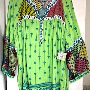 May include: A lime green tunic top with a V-neck and three-quarter sleeves. The top features a mix of patterned panels in yellow, teal, and burgundy. The neckline and cuffs are trimmed with white crochet. The top has a loose, flowing fit.