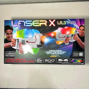 May include: A Laser X Ultra box set featuring two long-range double blasters. The blasters are white, with colorful accents and orange nozzles. The box includes the text "Laser X Ultra" and "The #1 Home Laser Tag System on the Planet!"