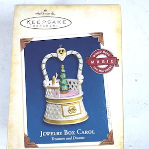 May include: A Hallmark Keepsake Ornament in a box. The ornament is a white and gold jewelry box with a Christmas tree inside. The box is labeled "Jewelry Box Carol" and "Treasures and Dreams". The box is from the Collector's Series.