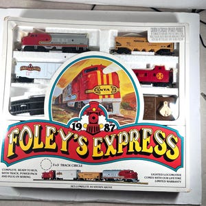 Könnte beinhalten: Ein Foley's Express Modelleisenbahn-Set in Originalverpackung mit einer rot-silbernen Santa Fe Lokomotive, einem gelben Morrison-Knudsen Wagen, einem weißen Foley's Express Wagen, einem roten Begleitwagen, Gleisen und einem Netzteil.