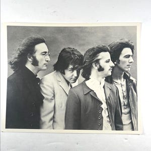 Può includere: Fotografia in bianco e nero di quattro uomini di profilo. Indossano giacche e camicie, con capelli lunghi e basette. L'immagine è una stampa vintage, probabilmente degli anni '60 o primi anni '70.