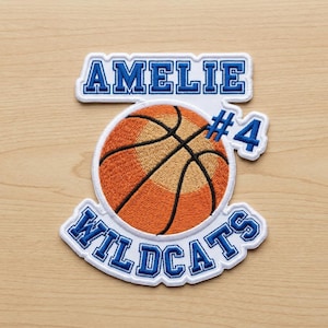 May include: Embroidered basketball patch with the name "AMELIE" above a basketball and the text "WILDCATS" below. The basketball is orange and brown with black lines. The text and border are blue and white.