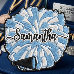 May include: A light blue and white embroidered pom-pom patch with the name "Samantha" in cursive script. A black megaphone is at the bottom. The patch is surrounded by a black border. Medals and a plaque that reads "Squad Excellence Team" are in the background.