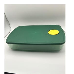 May include: A rectangular, green plastic food storage container with a matching green lid. The lid features a bright yellow, circular vent. The container is designed for food storage and organization.