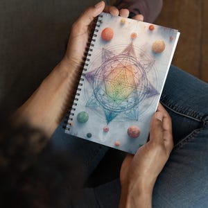 May include: Spiral-bound notebook featuring a geometric design with a rainbow center and surrounding spheres in various colors. The notebook has a white background and a black spiral binding.