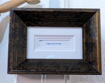 May include: A framed artwork with a dark brown and gold textured frame. The artwork features a white background with a recessed rectangular design. The text "Calgon, take me away!" is printed in blue.