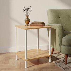 Può includere: Un tavolino laterale in legno chiaro con un ripiano inferiore e gambe bianche. Un vaso di ottone con lavanda secca e due libri sono sopra. Una poltrona verde sullo sfondo, creando uno spazio abitativo accogliente e dai toni neutri.