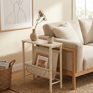 Può includere: Un tavolino laterale bianco sporco con un portariviste, un vaso beige con fiori secchi e una tazza. Il tavolo è accanto a un divano beige con un tappeto chiaro e un cesto di vimini.