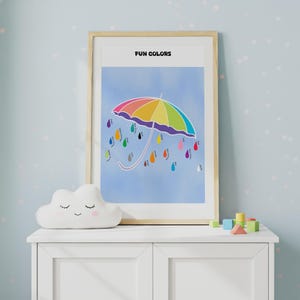 May include: A framed print with the text "FUN COLORS". The artwork depicts a rainbow umbrella with colourful raindrops on a blue backdrop. A white cloud-shaped cushion and wooden blocks are in the foreground, on a white cabinet.