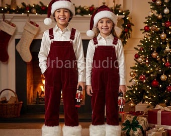 May include: Two children wearing matching burgundy corduroy overalls with white faux fur cuffs, white long-sleeved button-down shirts, and red Santa hats with white pom-poms. Each child holds a small wooden nutcracker figurine in their hand.