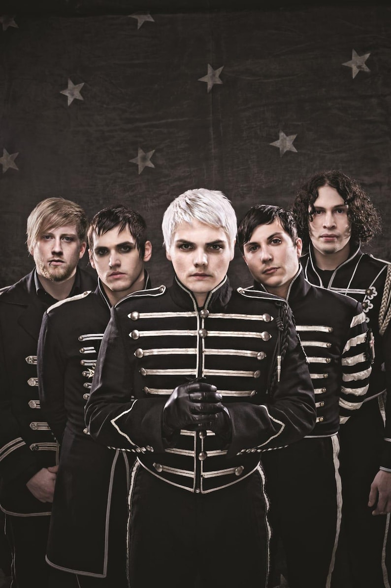 May include: Five individuals stand in a row wearing black military-style jackets with silver piping and buttons. The central figure has platinum blonde hair and black gloves. They are positioned against a dark backdrop featuring a star pattern.
