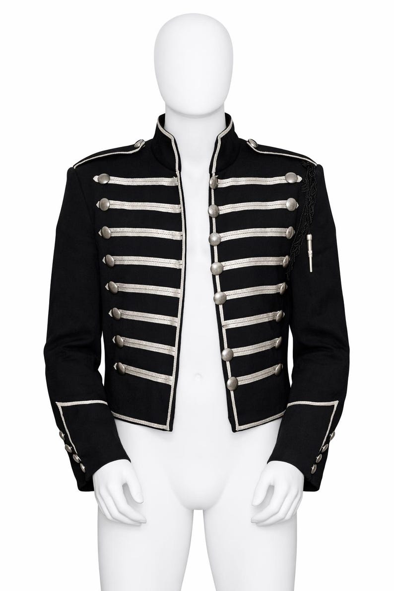 May include: A black military-style jacket featuring a high collar, silver-toned buttons, and horizontal silver piping across the front. The garment includes shoulder epaulets, long sleeves with buttoned cuffs, and decorative black braided trim.