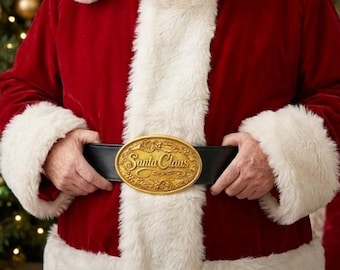 May include: A black belt featuring a large, oval-shaped gold-toned metal buckle with intricate embossed floral detailing and the words Santa Claus written in a cursive script across the center, worn over a red velvet coat with white faux fur trim.