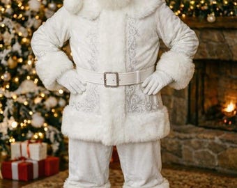 May include: A Santa Claus figure wearing a white velvet suit with silver embroidery, a matching hat, white faux fur trim on the cuffs and hem, a white belt with a silver buckle, white gloves, and white boots, standing with hands on hips.
