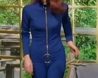 May include: A long-sleeved, deep blue jumpsuit featuring a high collar and a full-length silver-toned metal zipper down the front. The zipper pull is a large, circular metal ring positioned at the waist, creating a distinct focal point on the garment.