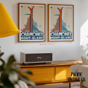 May include: Two framed vintage travel posters, each featuring a ski scene with the text "CHAMONIX MONT-BLANC". The posters are 24x36 inches and are mounted on a white wall. Below, a white and brown speaker with the name "Jimmy" sits on a wooden cabinet.