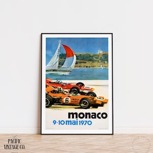 May include: Framed vintage poster featuring two race cars in orange and red, with the text "Monaco 9-10 mai 1970." A sailboat with a red and white sail is in the background, with a coastal scene.