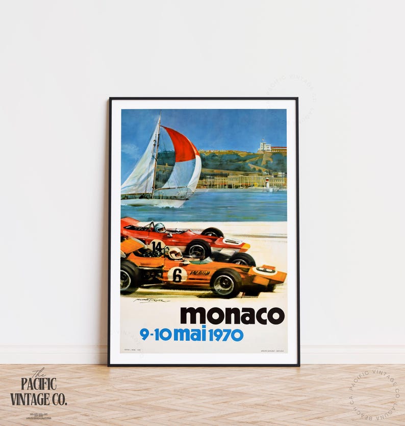 May include: Framed vintage poster featuring two race cars in orange and red, with the text "Monaco 9-10 mai 1970." A sailboat with a red and white sail is in the background, with a coastal scene.