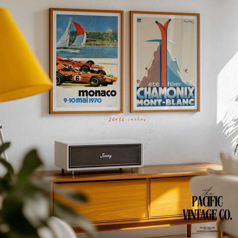May include: Two framed vintage travel posters, one for Monaco and the other for Chamonix Mont-Blanc, each 24x36 inches. The Monaco poster features race cars and a sailboat. The Chamonix poster shows skiers and a mountain scene. A white and brown speaker sits below.