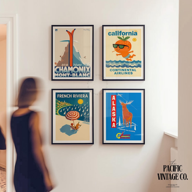 May include: Four framed vintage travel posters on a white wall. The posters feature destinations like Chamonix, California, French Riviera, and Alaska. Each poster has a black frame and colorful illustrations, evoking a retro travel aesthetic.