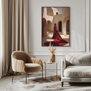 Peut inclure: Une impression d'art mural encadrée représentant une silhouette drapée dans un long vêtement rouge profond et fluide, se tenant au milieu d'une série d'arches en pierre beige. La scène capture une architecture désertique avec des ombres douces.
