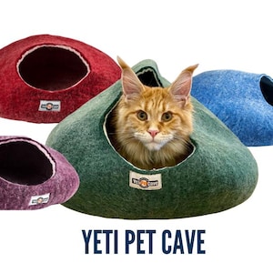 May include: A ginger cat peeks out of a green felt pet cave, with three other felt caves in red, purple, and blue. The text "YETI PET CAVE" is displayed below the caves. These cozy pet beds are designed for cats.