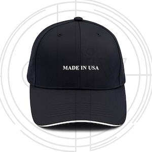 Puede incluir: Gorra de béisbol negra con visera curva y ribete blanco. El texto "MADE IN USA" está impreso en blanco en la parte delantera. La gorra tiene un diseño estructurado y una corona redondeada.