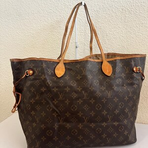 Könnte beinhalten: Eine braune Tragetasche mit dem ikonischen Louis Vuitton Monogramm-Muster in Gold, Hellbraun und Dunkelbraun. Die Tasche verfügt über zwei dünne, hellbraune Leder-Schulterriemen, goldfarbene Metallbeschläge und seitliche Kordelzüge zur Weitenregulierung.