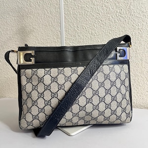 Puede incluir: Bolso de hombro vintage con un patrón de monograma GG azul y gris. El bolso presenta una parte superior y una correa de cuero negro, con herrajes plateados y un acento azul. El bolso es rectangular y tiene una correa larga y ajustable.