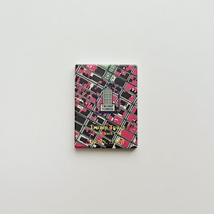 May include: A rectangular magnet with a geometric pattern in black, pink, and white. It features the Trump Tower logo and the text "Trump Tower New York, NY". The design has a grid-like appearance.