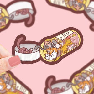 May include: A whimsical sticker featuring a pill bottle overflowing with cartoon cats of various colors. The cats are inside the bottle and the cap, with a prescription label. The sticker is held by a hand with a pink nail.