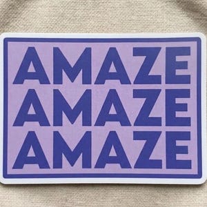 May include: A rectangular sticker with a white border and a light purple background. The word "AMAZE" is printed in dark blue, repeated four times in a stacked layout.