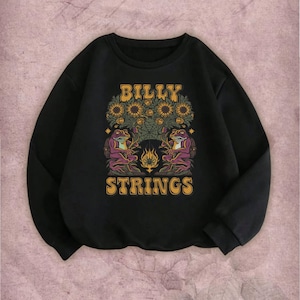 May include: Black sweatshirt with a graphic design featuring the text "BILLY STRINGS" in gold lettering. The design includes sunflowers, two purple frogs, and a flame. The sweatshirt has long sleeves and a crew neck.