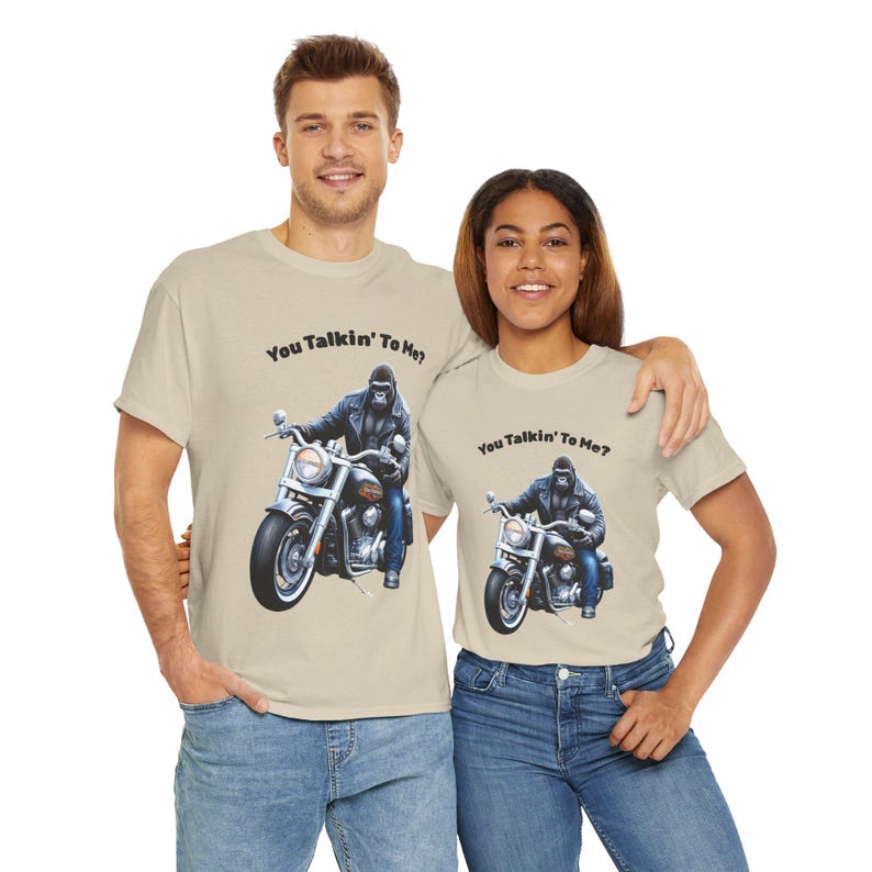 K&ouml;nnte beinhalten: Beige T-Shirts mit dem Text "You Talkin' To Me?" und einer Grafik eines Gorillas auf einem Motorrad. Der Gorilla tr&auml;gt eine Lederjacke und blaue Jeans. Ein Mann und eine Frau tragen die T-Shirts.