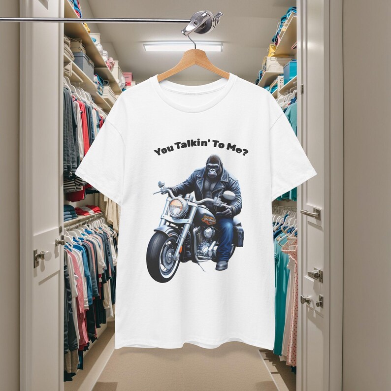 K&ouml;nnte beinhalten: Wei&szlig;es T-Shirt mit einem Gorilla auf einem Motorrad. Der Gorilla tr&auml;gt eine Lederjacke und Jeans. Der Text "You Talkin' To Me?" ist &uuml;ber dem Motiv aufgedruckt. Das T-Shirt h&auml;ngt an einem Holzb&uuml;gel.