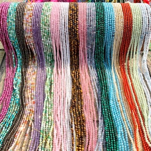 May include: A selection of beaded necklaces in a variety of colours, including pink, green, purple, and brown. The small beads are strung together, creating a textured surface. The necklaces are displayed side by side.
