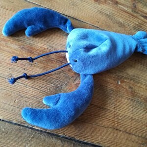 May include: A blue plush lobster toy with a soft, velvety texture. The lobster has two large claws and a long tail.