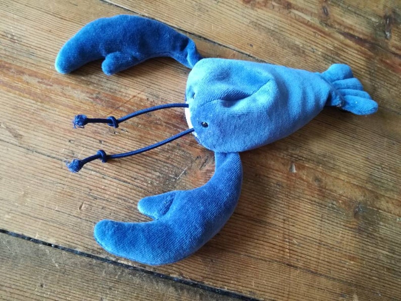 May include: A blue plush lobster toy with a soft, velvety texture. The lobster has two large claws and a long tail.