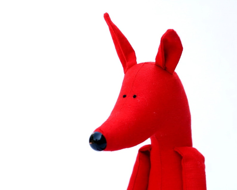 May include: A red fabric toy shaped like a fox with black eyes and a black nose.