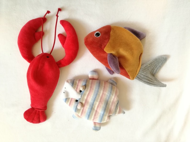 May include: Three plush toys: a red lobster, a striped fish, and an orange and purple fish.