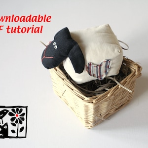 May include: A black and white sheep plush toy with a red heart on its side, sitting in a wicker basket. The text "Downloadable PDF tutorial" is visible at the top of the image.