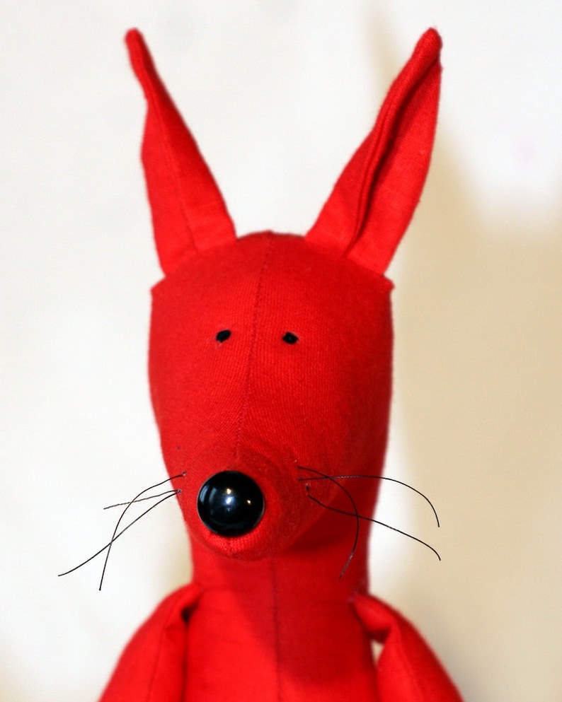 May include: A red plush toy with long ears, a black nose, and black whiskers. The toy is made of soft fabric and has a simple design.