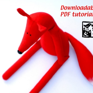 May include: Red fabric fox toy with a white tipped tail.  The fox is sitting on a white surface.  Downloadable PDF tutorial.