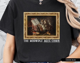 Pode incluir: T-shirt preto com uma pintura emoldurada de gatos cantando com partituras. A pintura está em uma moldura dourada e o texto "THE MEOWDLE AGES CHOIR" está abaixo. A camisa faz parte da coleção "ART HISTORY SERIES - T-SHIRT".