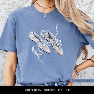 May include: A blue jean coloured t-shirt with a print of two vintage satin shoes with bows and ribbons. The text "VICTORIANS SERIES - T-SHIRT" is at the bottom. The shirt's colour is labelled as "BLUE JEAN".